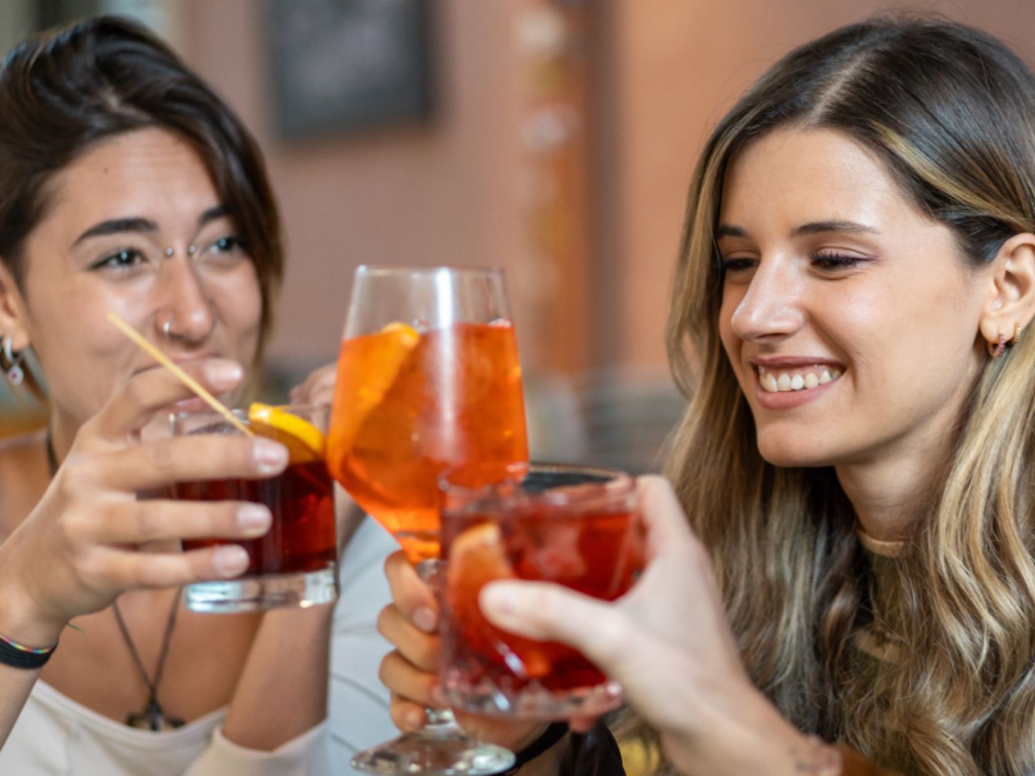 Zwei lächelnde Menschen stoßen in entspannter, geselliger Atmosphäre mit bunten Cocktails an.