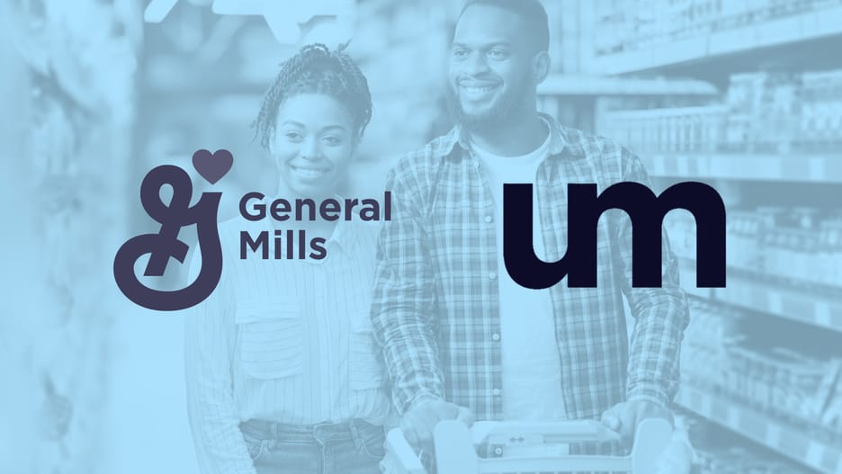 Smiling adult couple shopping together in a grocery store aisle, pushing a cart filled with items.