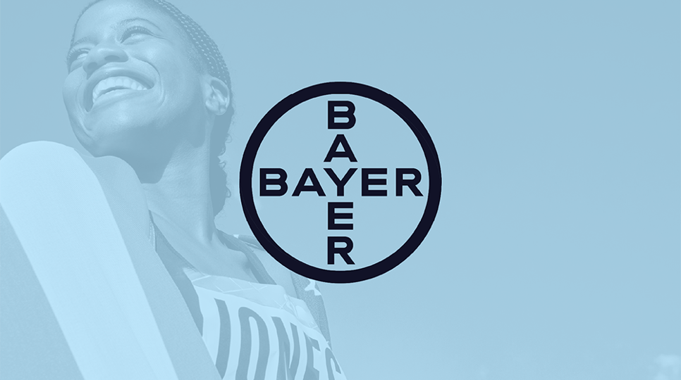 An olympian smiling and wrapped in the American flag with a blue overlay and the Bayer logo in the center