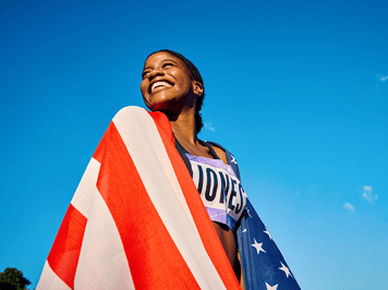 An olympian smiling and wrapped in the American flag